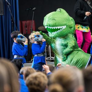 Student dinosaurs next to a green dinosaur at a JAM Band performance in Adelaide South Australia